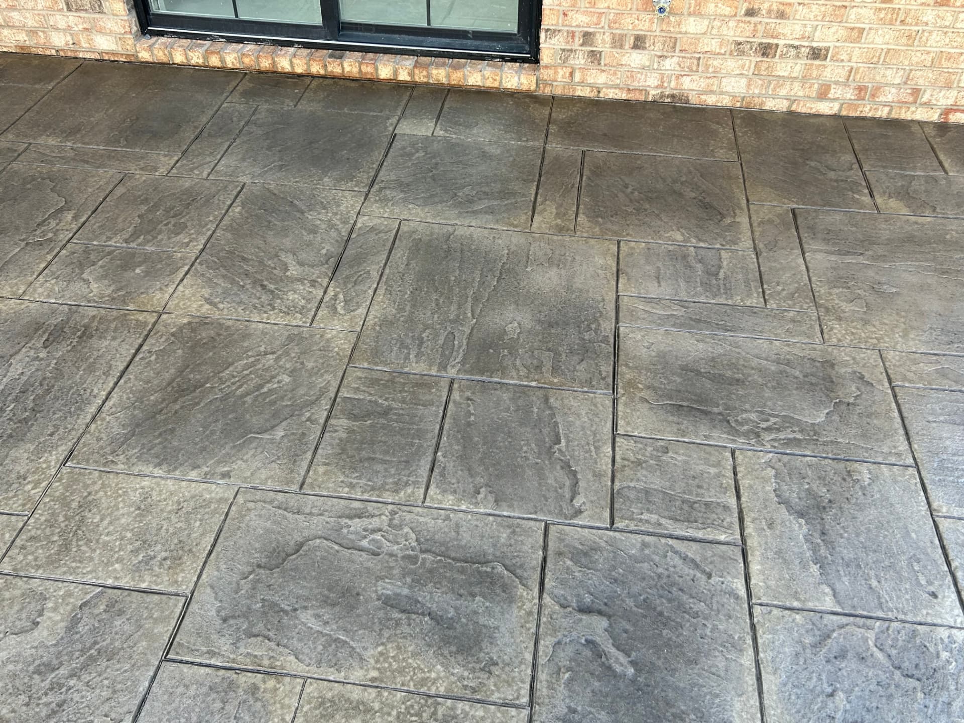 Gray slate stamped concrete patio beside a brick home
