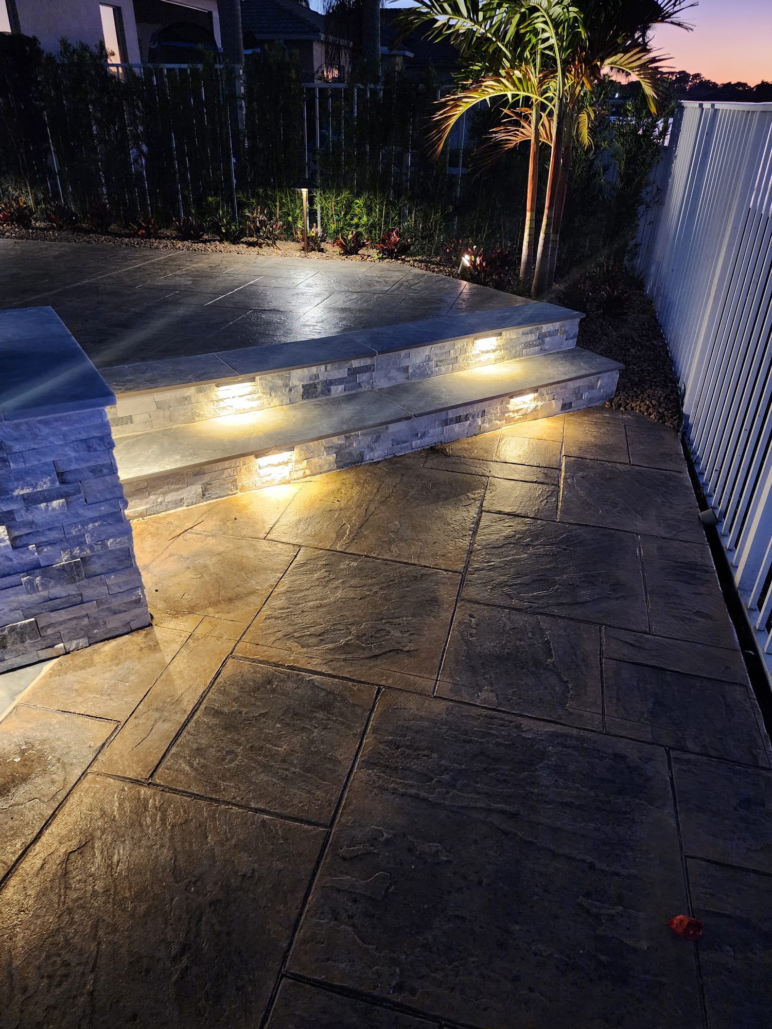 Stamped concrete patio with lit stone-faced steps at dusk