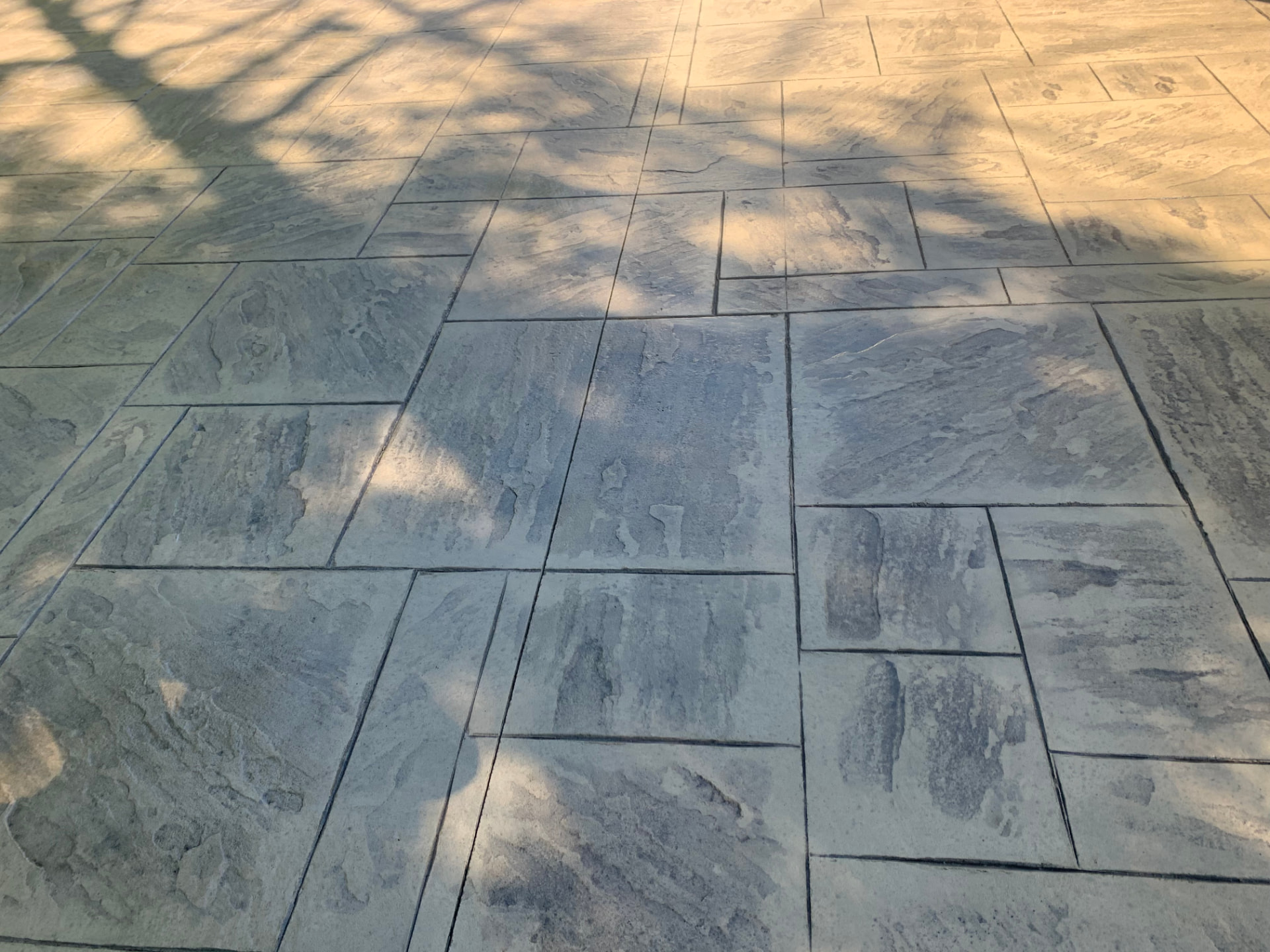 Blue and tan ashlar stamped concrete patio in dappled shade