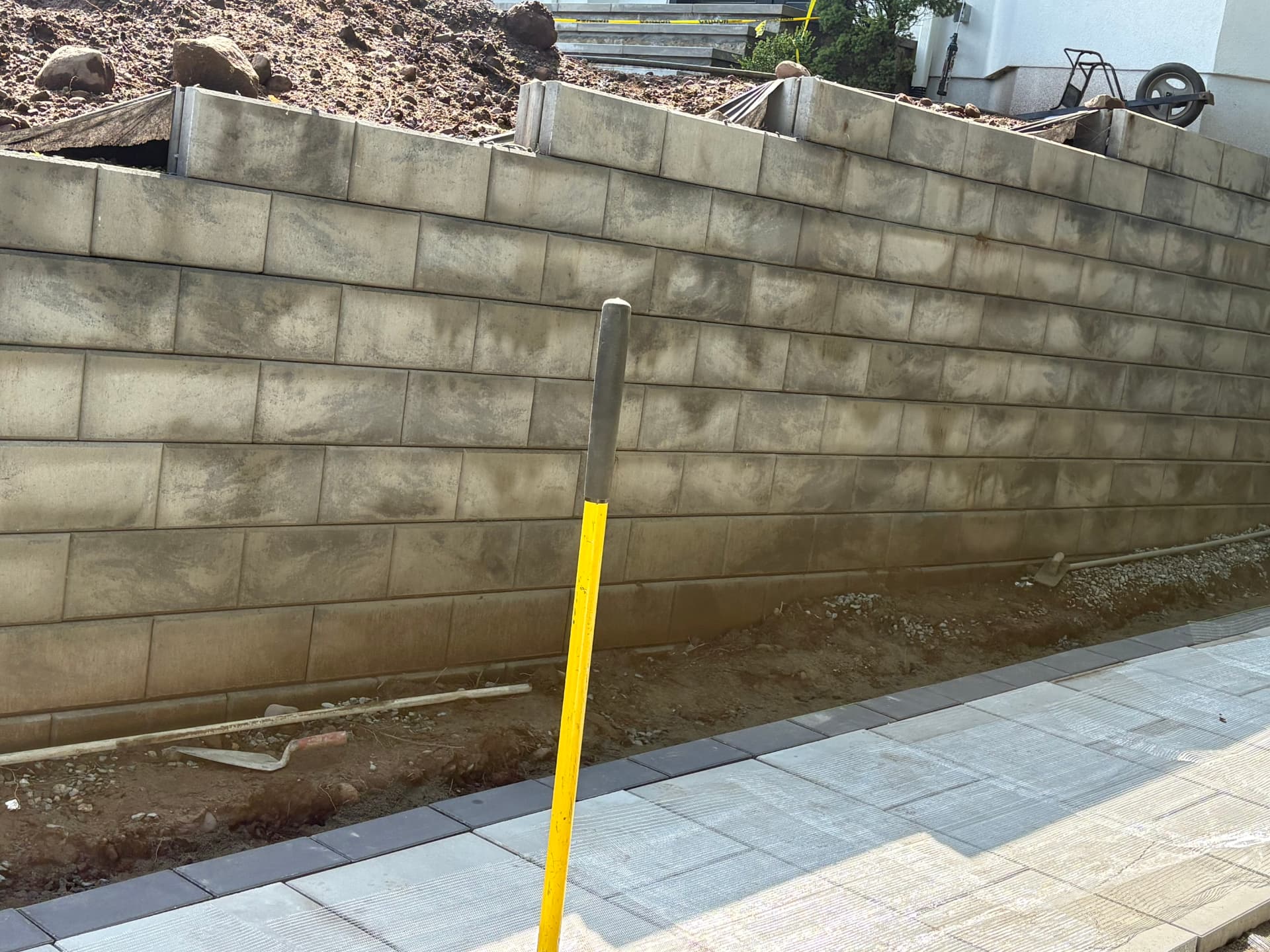 Tan segmental block retaining wall beside a new paver walkway