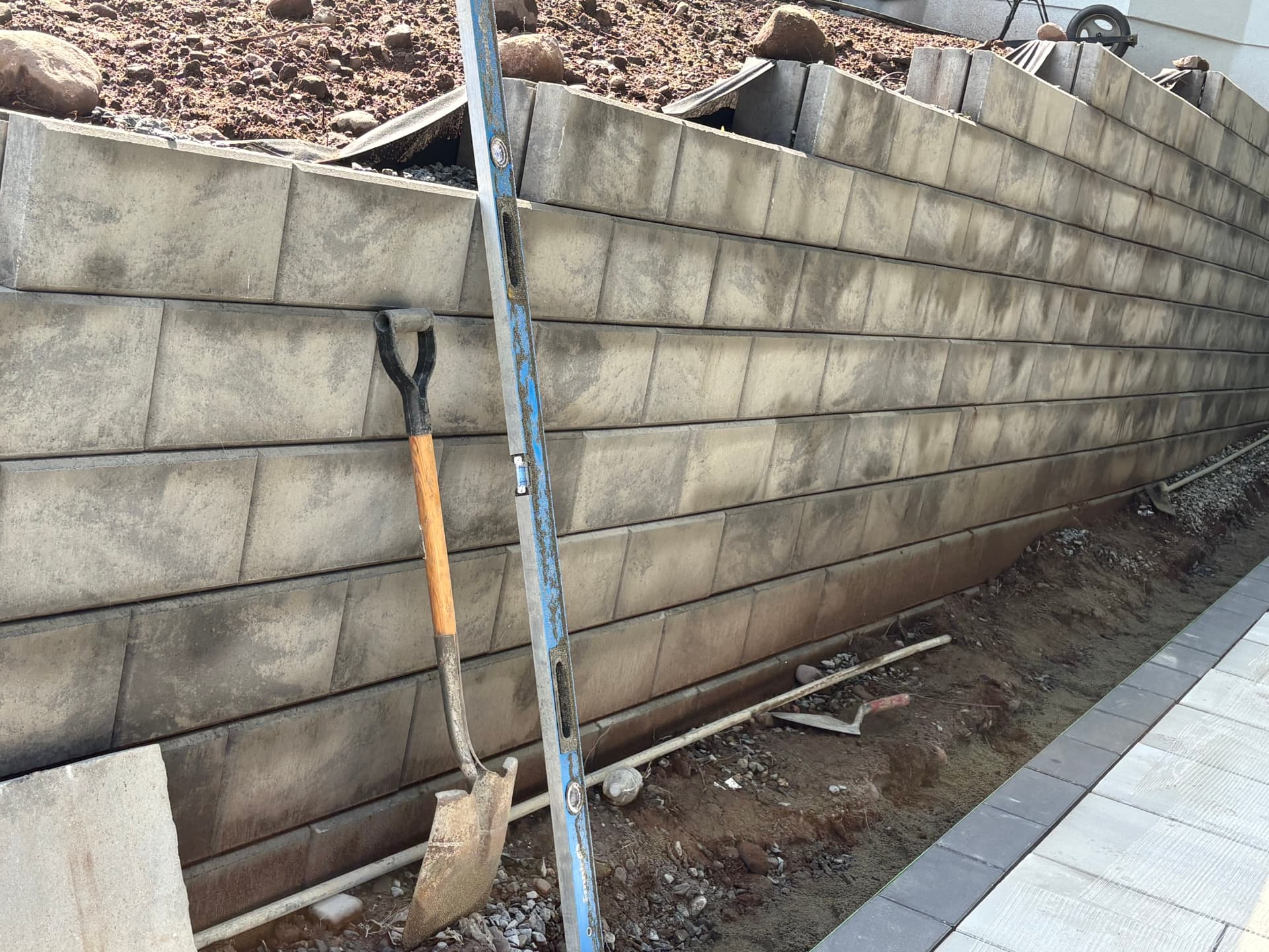 Segmental block retaining wall under construction with level and shovel