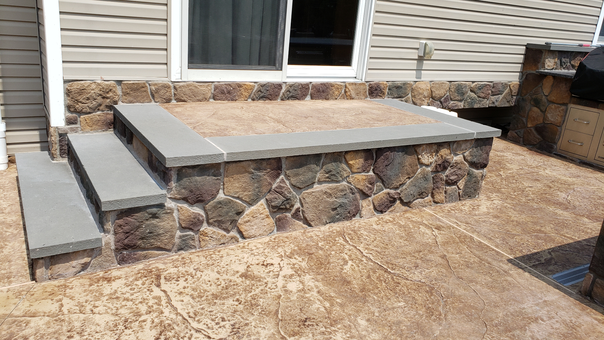 Stone veneer landing with bluestone cap on stamped patio